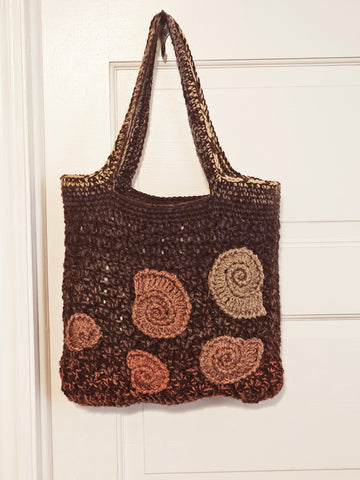 Crocheted brown tote bag with spiral shell-like decorations in lighter shades.