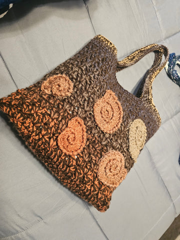 Crocheted brown tote bag with spiral shell-like decorations in lighter shades.