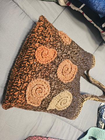 Crocheted brown tote bag with spiral shell-like decorations in lighter shades.