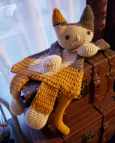 Crocheted cat-like stuffed toy with gray, yellow, and white yarn.