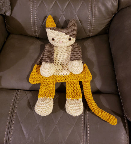 Crocheted cat-like stuffed toy with gray, yellow, and white yarn.