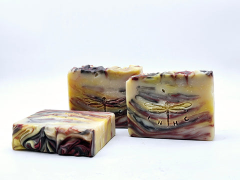 Three handmade soap bars with swirled patterns and dragonfly logos.